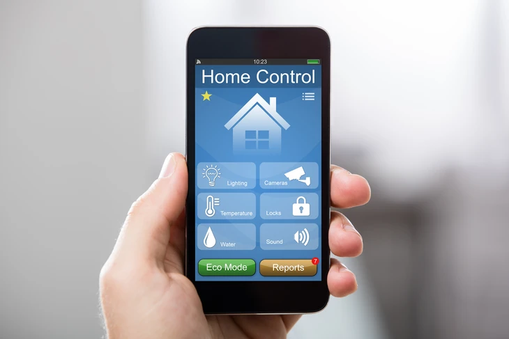 Main tenant un smartphone affichant une application de domotique "Home Control" avec interface bleue