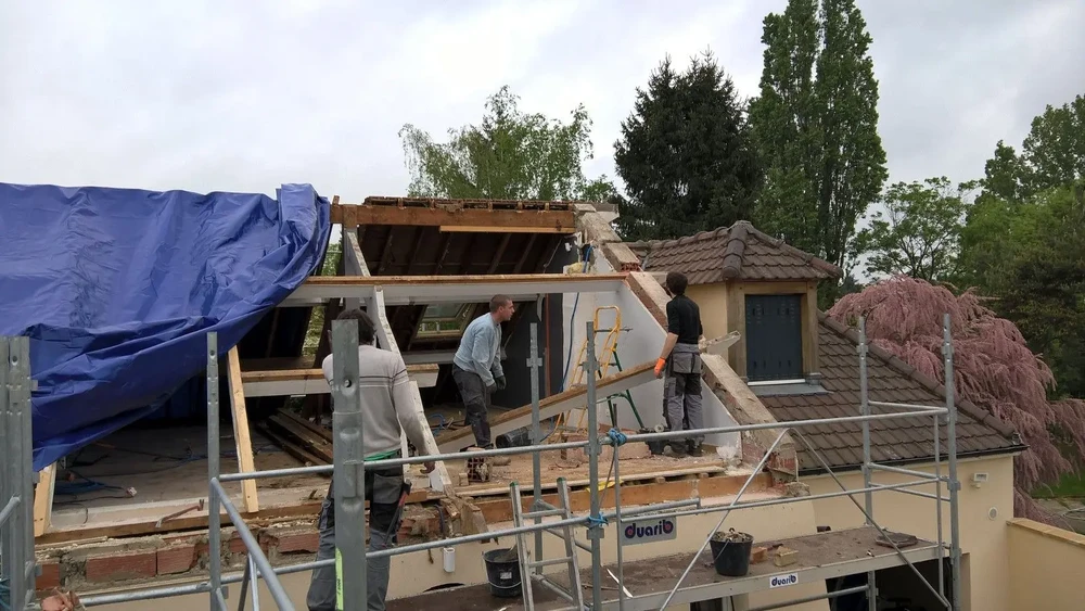 Chantier de construction extérieur avec ouvriers installant une charpente en bois sur maison résidentielle