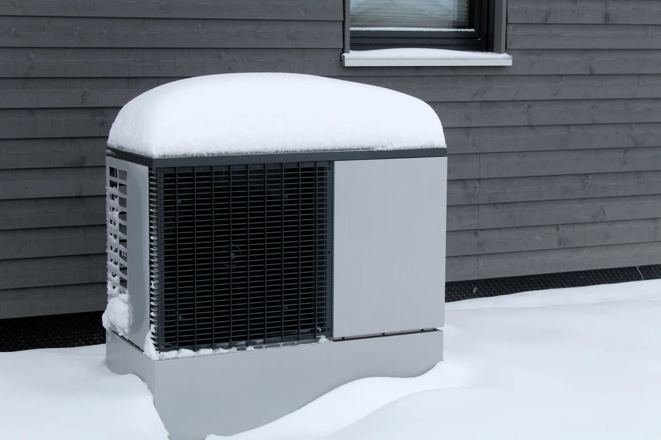 Extérieur résidentiel hivernal avec unité de climatisation/pompe à chaleur recouverte de neige