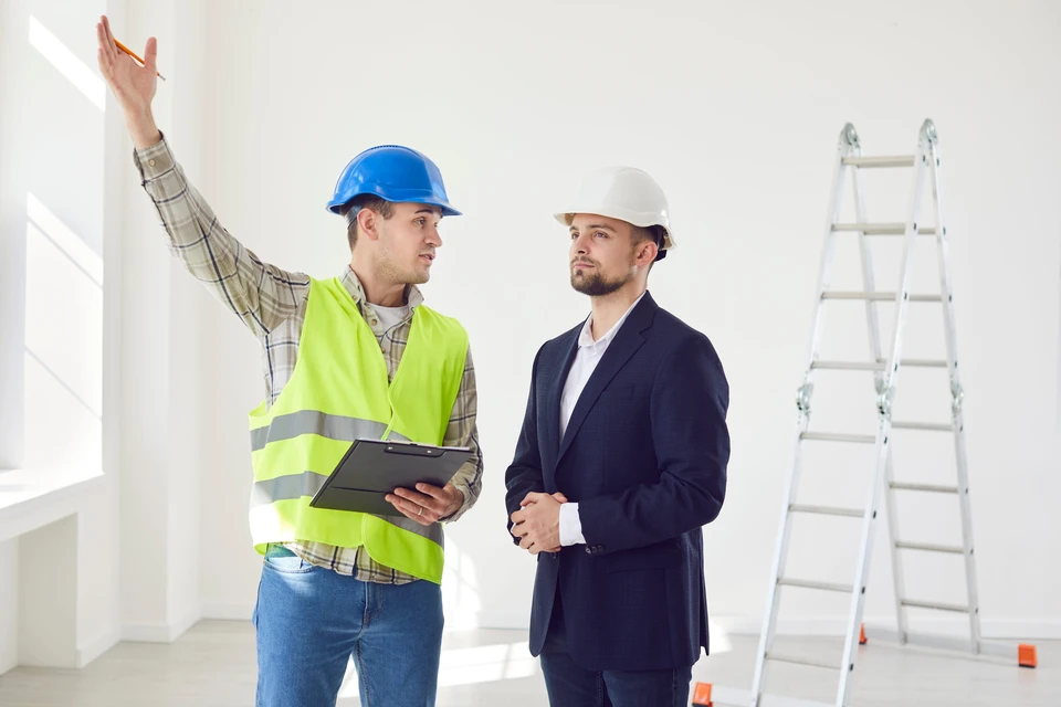 Contrema&icirc;tre discutant avec le jeune projet de conception d'architecte ou de r&eacute;paration d'un nouvel appartement debout dans une pi&egrave;ce blanche vide sur le chantier de construction
