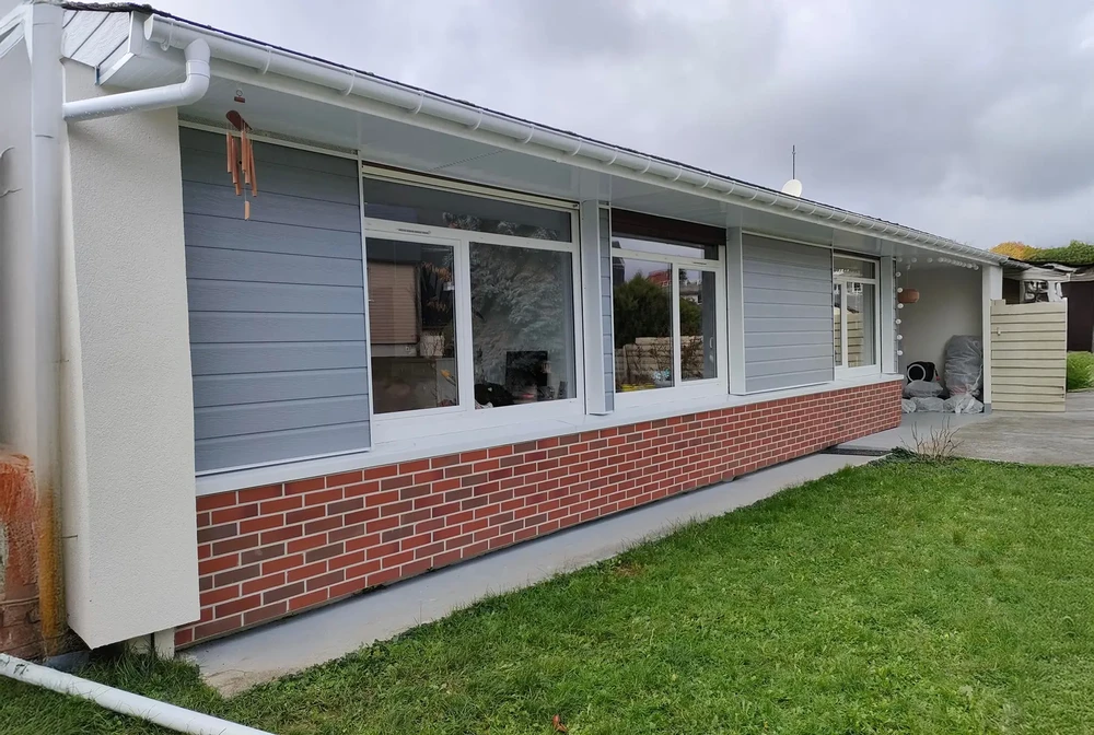 Façade extérieure de maison individuelle moderne avec mur mixte briques rouges et bardage horizontal gris-bleu