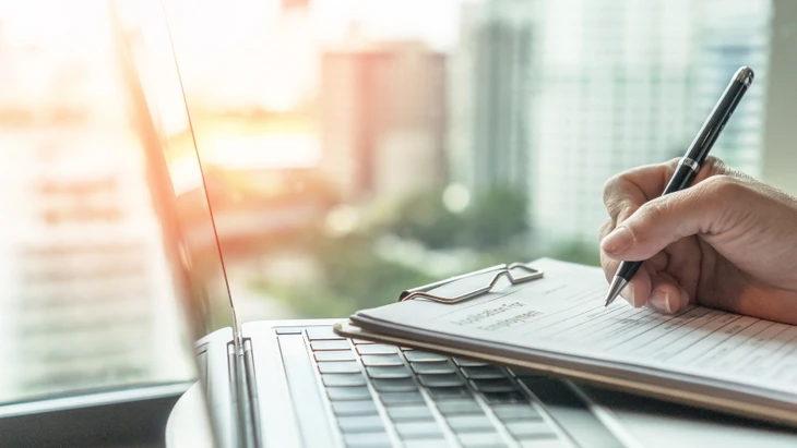 Un ouvrier en gilet de sécurité orange et casquette noire consulte une tablette numérique sur un chantier de construction